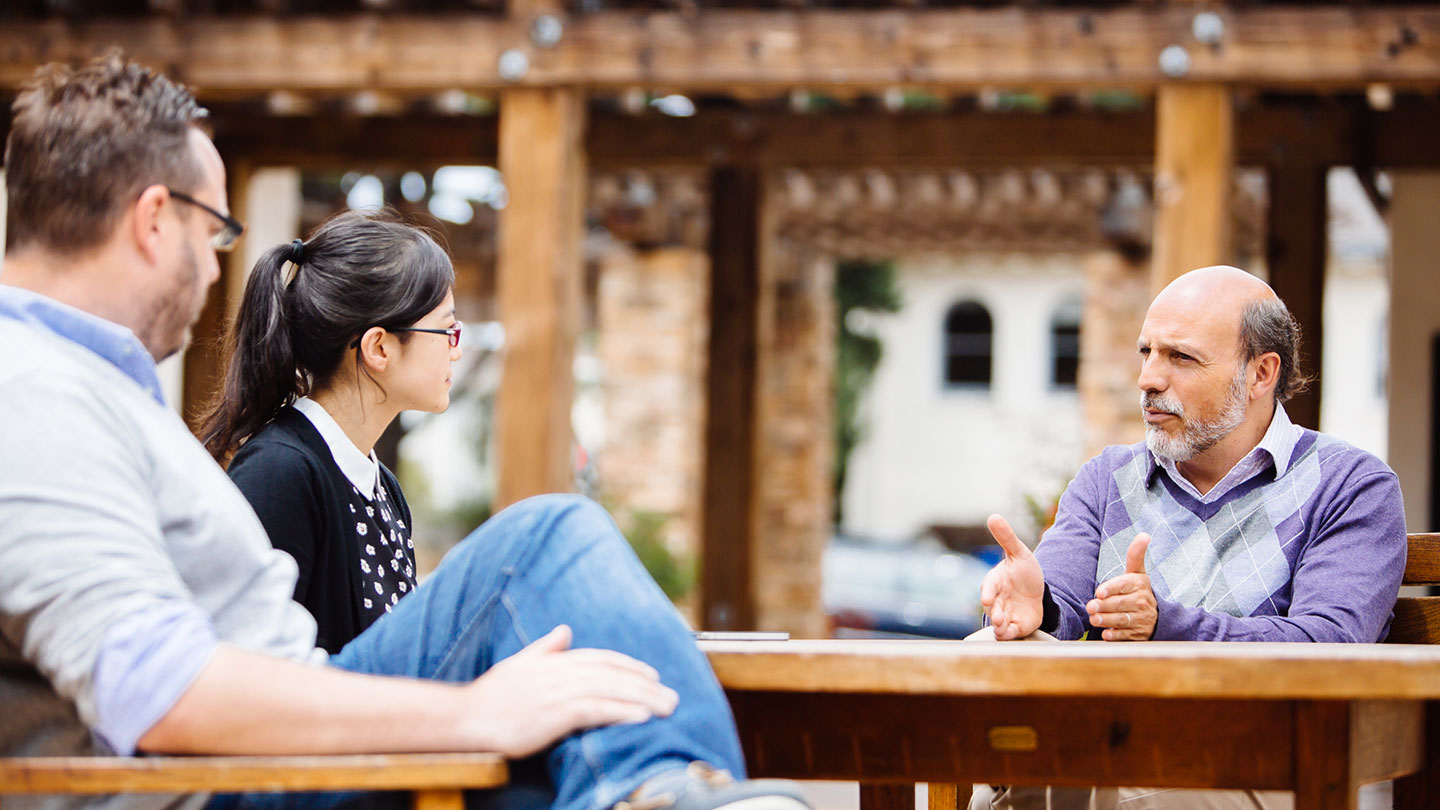 Professor Arrocha in discussion with two students outside at a table.