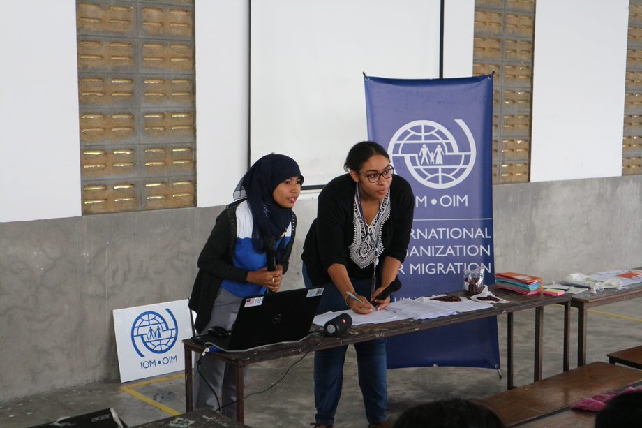 Two women standing by a table taking notes behind an IOM poster