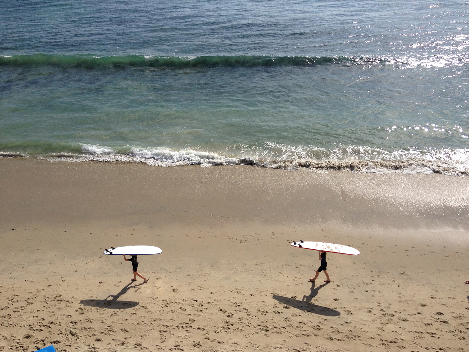 Two ladies walking on beach with surfboards balanced on their heads