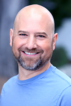 Dr. Jason Scorse in a blue tshirt with a smiling face, bald head, and beard