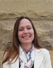 Dr. Anna Carolina Muller Queiroz, researcher with the Lemann Center at Stanford University with smiling eyes and smiling face, long brown hair, wearing a white sport coat and neat scarf