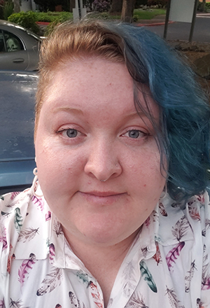 CBE Summer Fellow 2021-Louise Shurvinton Bradley-wearing a cute blouse with multicolored feathers on it, and looking smart and sassy with blue hair