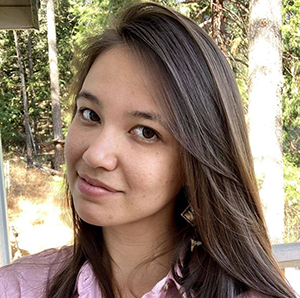 CBE Summer Fellow 2021-Sarah Wickman-with a look on her face that says "don't mess with me" in a sassy, friendly way, long brown hair, pinkish blouse, in a grove of aspen trees