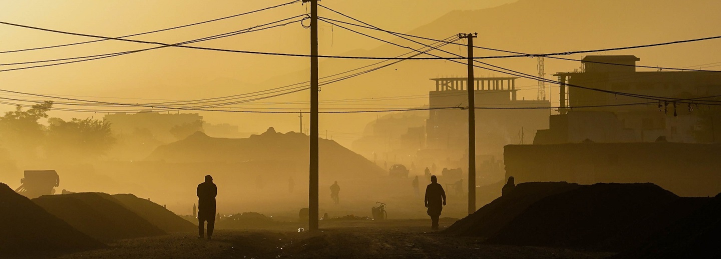 Two silhouettes of people walking against a dusty skyline bathed in the yellows and oranges of dawn