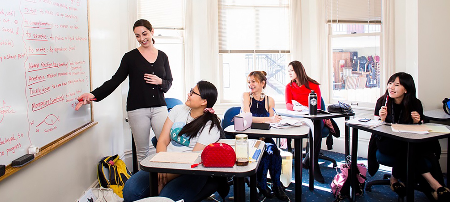 Young woman pointing at a whiteboard as she teaches four students