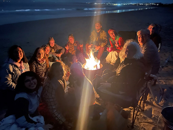 A group of vaccinated people sit around a beach bonfire on Del Monte Beach, Monterey, CA