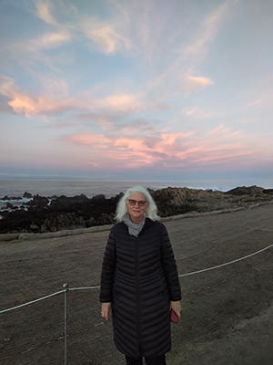Dr. Kristina Gjerde standing on the rocky coastline of Pacific Grove, with an incredible January 2022 sunset