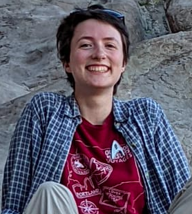 A bright smile from Mallory Hoffbeck, looking pleased, sitting on a mountain boulder