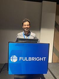 Diego Tabilo, standing and smiling brightly at a podium lectern, which bears the word "Fulbright" and the Fulbright logo