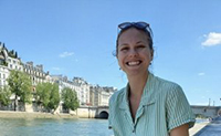 Hannah Ditty smiling brightly with the banks of River Seine (Quais de la Seine) in Paris behind her