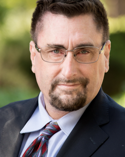 Anthony Castelletto in a business suit, glasses, mustache and goatee, smiling and looking serious