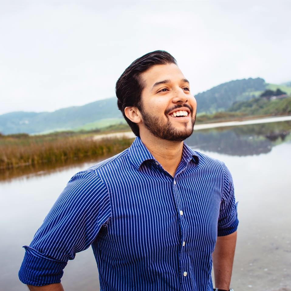 A photo of William Billy Holness smiling with beautiful mountain lake scenery in the backgroound