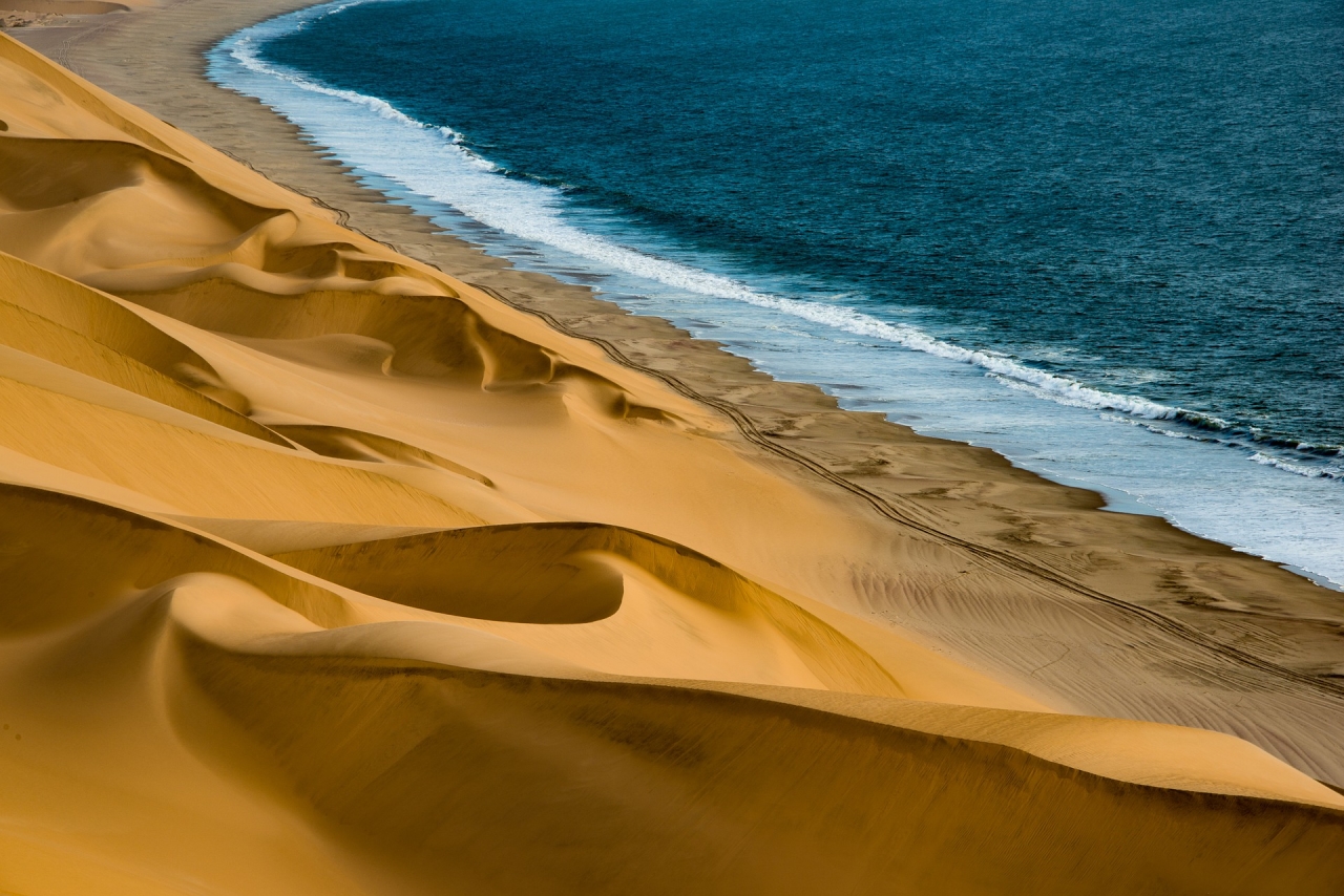 Striking image of golden, swirling sand dunes dropping off to blue ocean