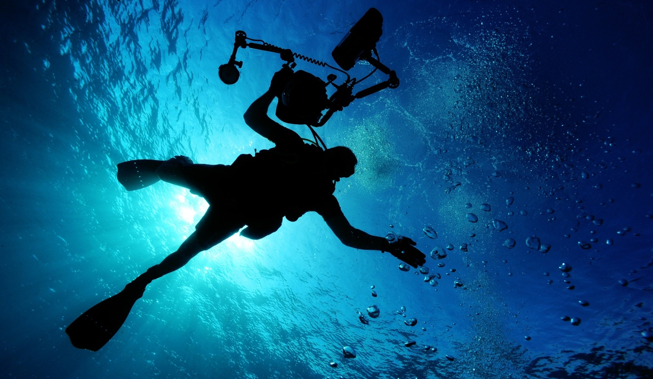 Scuba diver in blue ocean with light from behind slash above