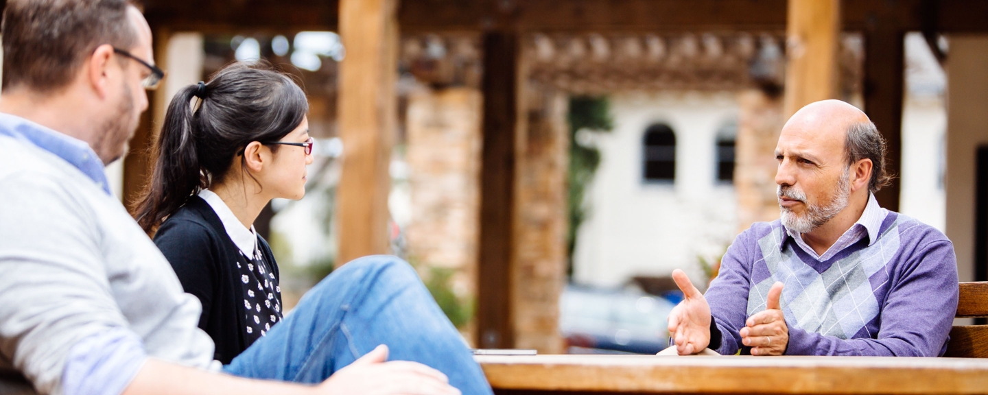 Professor Arrocha in discussion with two students outside at a table.