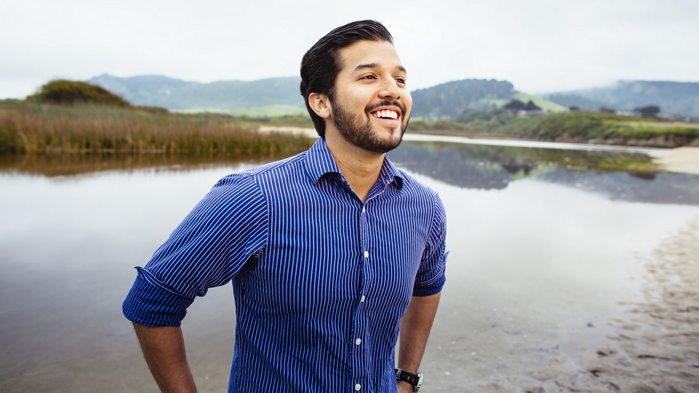 William Franco, international environmental policy alumnus, smiling and standing outside by a marsh in Monterey