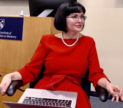 A woman in a red dress Dr Gaman Golutvina sits in a chair in front of a podium