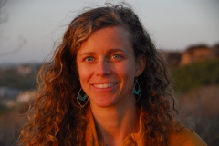 Headshot of Mandy Sackett, smiling, outside in nature, looks like a dune or beach cliff, in light of setting sun