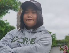 Emily Hoang looking at the camera with her arms folded, wearing a CORE hoodie and cap