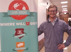 Daniel Watson standing next a banner from the University of Utah Learning Abroad program.