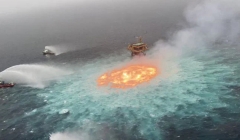 Grey skies and the Gulf of Mexico showing a ring of fire (orange) on the turquoise sea, with fire boats (red) trying to dowse the flames from a gas leak by nearby oil platform (red)