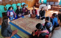 Group of people sitting cross-legged on the floor around a rectangular carpet.