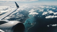 View of an airplane wing and engine from inside a flying plane with a beautiful coastline and clouds in the background