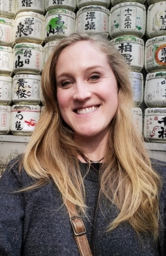 Aimee Kerr, smiling and looking kind, standing in front of a shelf of Japanese labeled cans