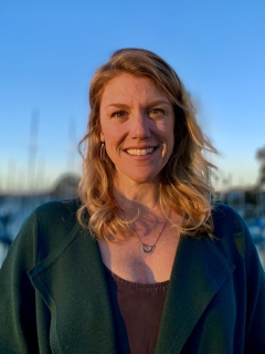 Sra Pfeifer smiling into a setting sun, a warm smile, warm light, and a marina with sailboats behind her