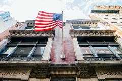Photo of an American flag hanging from a building waving in the breeze.