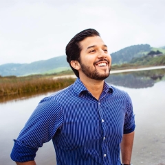 A photo of William Billy Holness smiling with beautiful mountain lake scenery in the backgroound