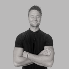 Teej Ragsdale with arms crossed looking strong in a black t-shirt, a smile and direct look at camera, short black hair