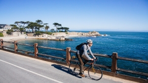 A young man riding his bike along the ocean near Monterey.