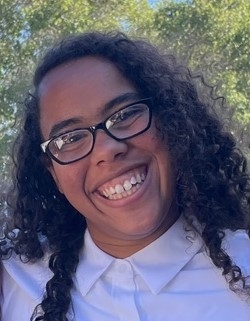 Photo of smiling Isha Banks, black hair, black glasses, white shirt