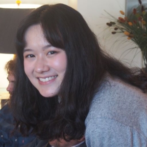 photo of Wenlan Zhang, smiling, black hair, grey sweater with flowers behind her