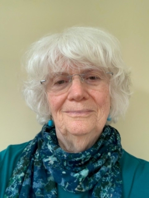 Judy Kildow, older woman smiling with glasses, blue scarf, blue shirt, blue earrings. 