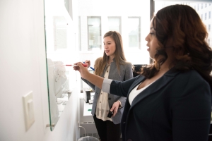 Two co-workers looking and writing on a whiteboard
