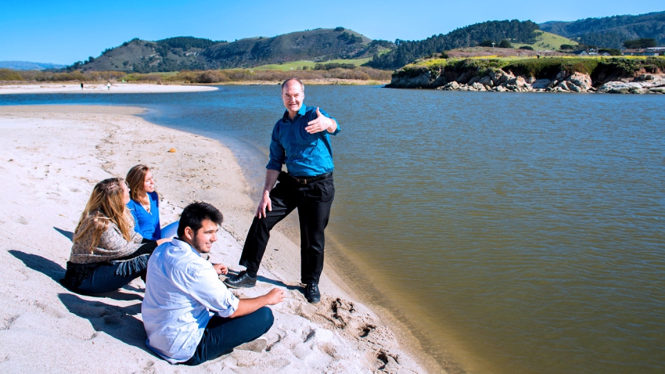 A professor and several students discuss sustainability issues along the shoreline at a beach in Monterey Bay.