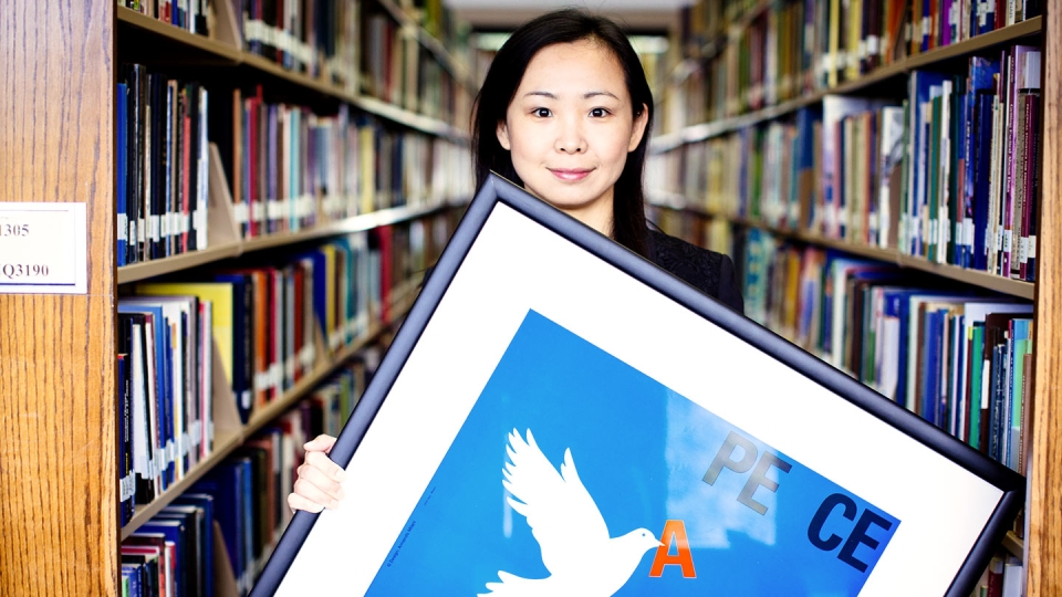 A young woman holds a poster that says "Peace" with a white dove on a blue background.