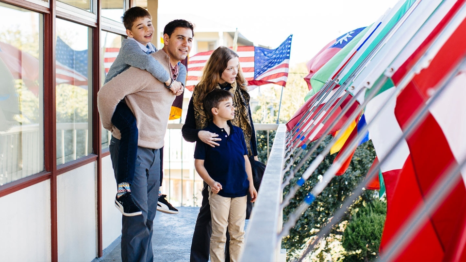 A father, mother and two sons stand on a blacony among world flags.