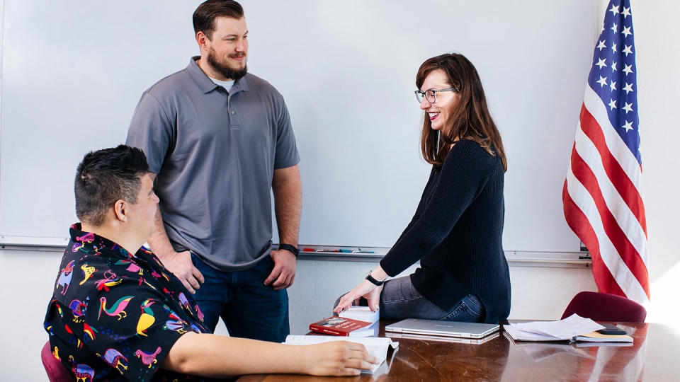 Two male students and a female student talk in a classroom.