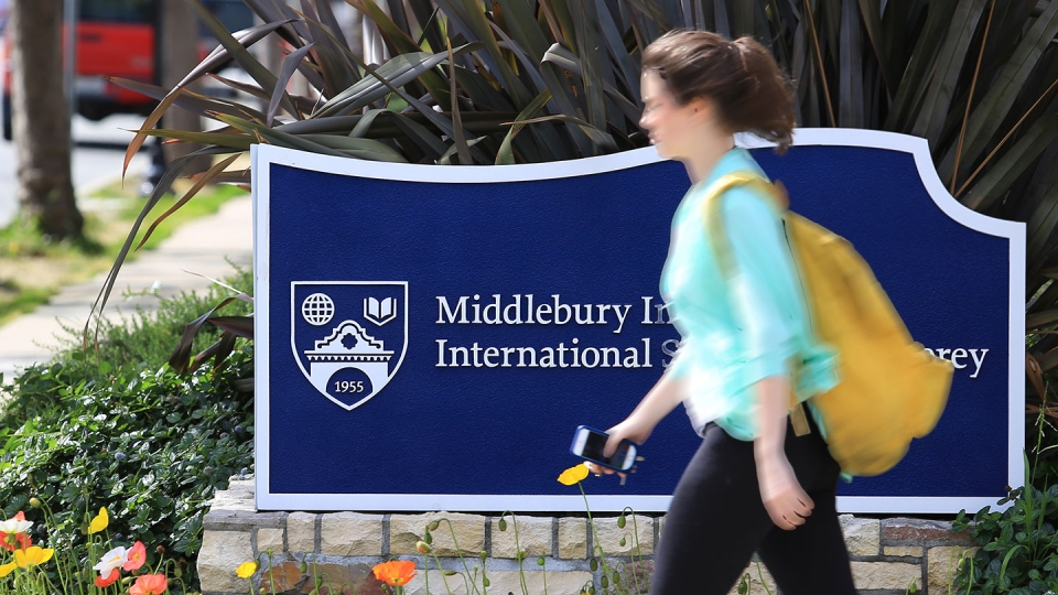 A young female student walks on campus in front of an Institute sign.