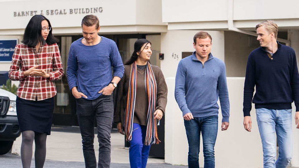 Two female and three male students walk across a parking lot.