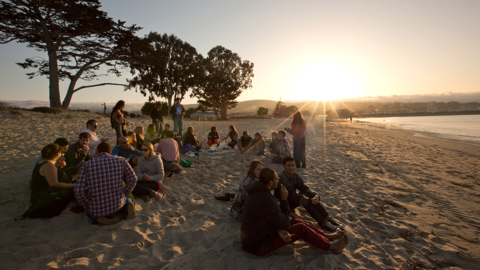 Students gather on the beach during sunset