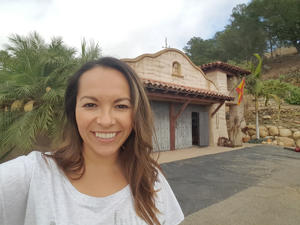 Mrs. Silvia Bor, smiling and standing in front of a mission style historic building