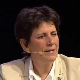 Dr. Barbara Block, looking intent and speaking against a black background, with wireless mic across her cheek, and wearing a tan blazer, white collared shirt