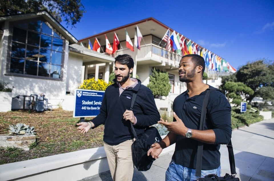 Two students walking in front of Morse (a building on campus decorated with flags of several countries)