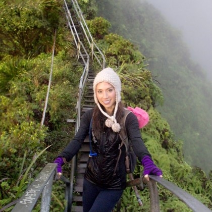 Ms. Joy Shih, on a misty day in Hawaii, crossing a long wooden path, she is smiling, wearing a black coat, and warm white cap, purpe gloves