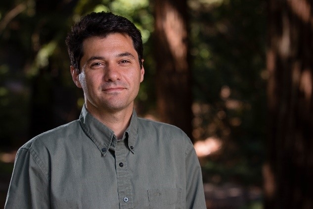 Juliano Calil a youngish man with dark hair, green button up shirt, smiling with his eyes, but mouth shut