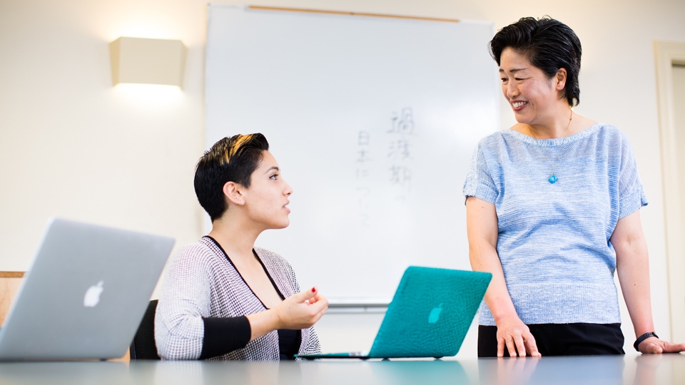 Student sitting at computer with teacher standing
